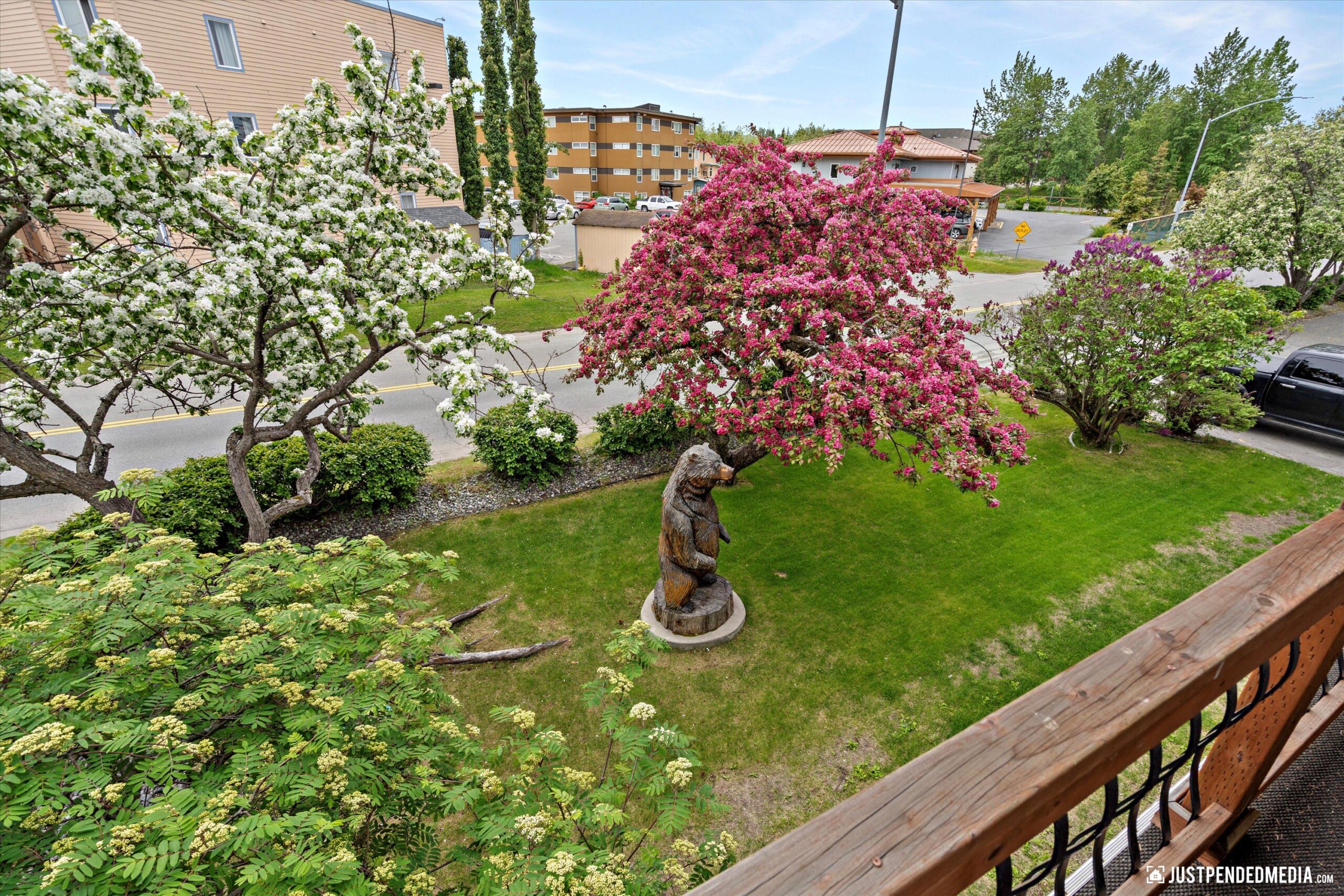A green outdoor yard area, surrounded by lush trees featuring a wooden bear sculpture
